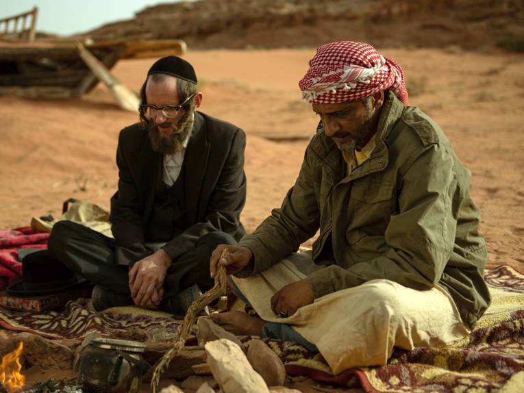 zwei Männer – einer mit Kippa, der andere mit Palästinensertuch – sitzen in der Wüste am Lagerfeuer